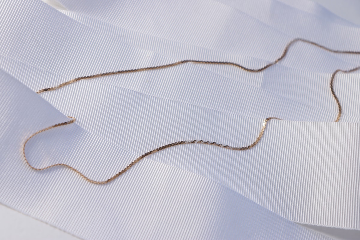 Fins colliers à chaîne en bijoux acier inoxydable ton or posés sur un tissu plissé blanc