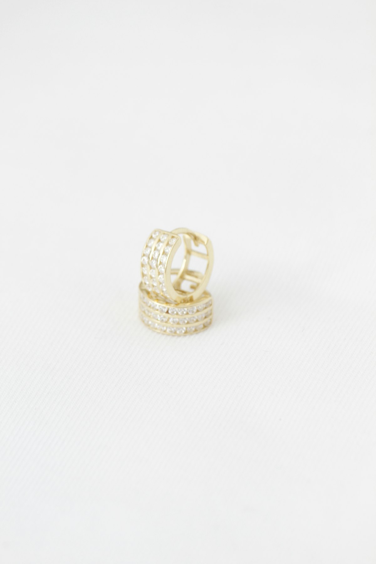 A single pair of gold-tone huggie hoop earrings set with small clear pave stones on a white surface