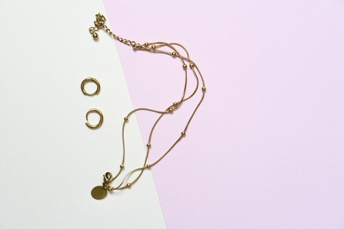 Gold-tone huggie hoop earrings and layered chain necklaces on a pastel background