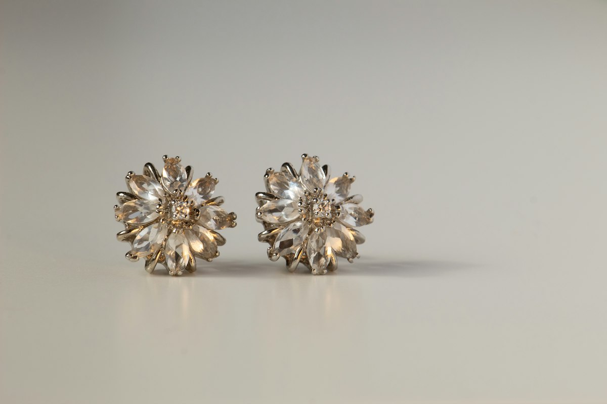 Pareja de pendientes de flor color plata con piedras transparentes sobre superficie gris clara