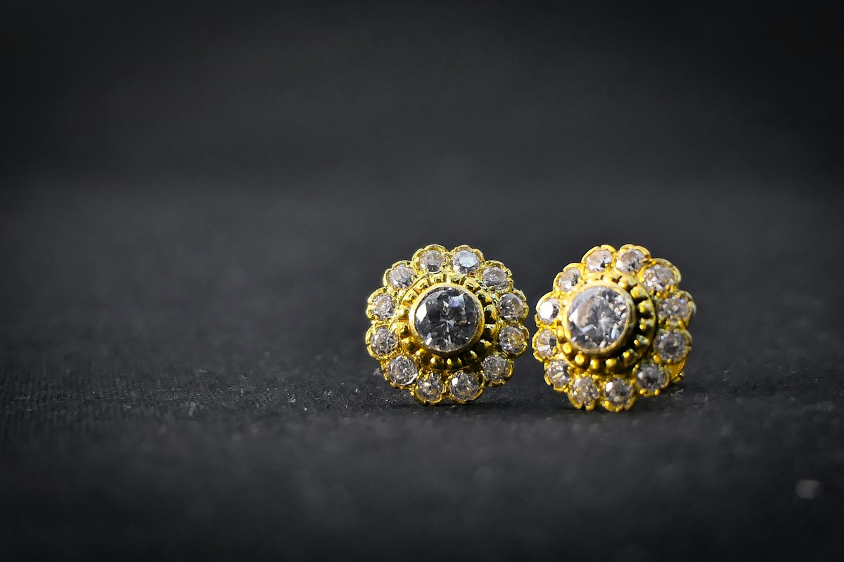 Pareja de pendientes de botón agrupados color dorado con piedras transparentes sobre tela oscura