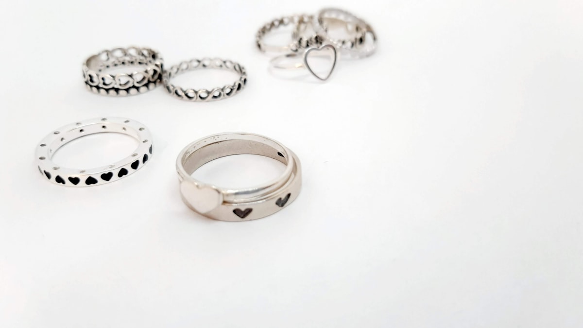 Several silver-tone rings with heart motifs and darkened detailing, arranged on a plain white background