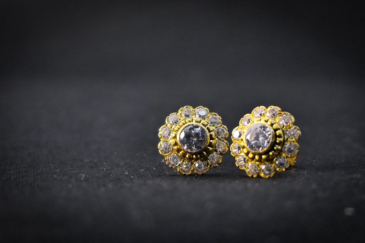 Close-up of a pair of gold-tone stud earrings with clear stones on a dark fabric surface