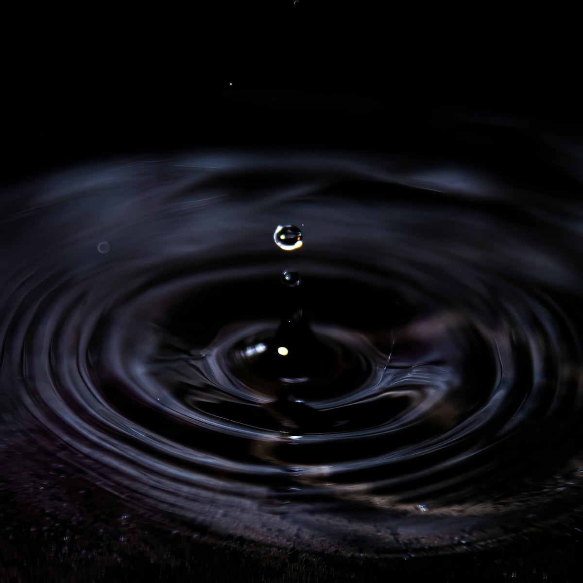 Una gota de agua que forma ondas sobre una superficie oscura